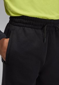 Calças de fato de treino pretas com cintura elástica, cordão ajustável e bolsos laterais, confeccionadas em tecido macio para maior conforto.