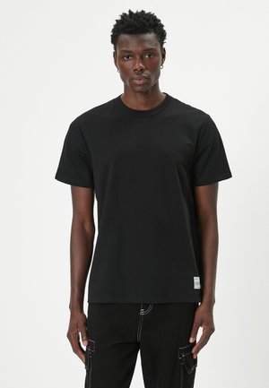 Camiseta de algodón negra con un corte clásico, mangas cortas y cuello redondo acanalado. Presenta una pequeña etiqueta en el dobladillo.