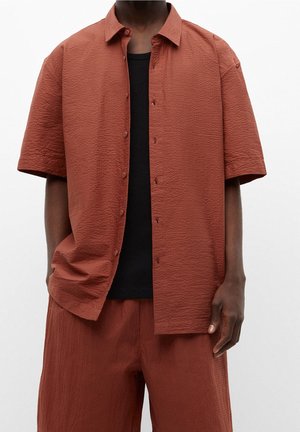 Zweifarbiges kurzärmliges Hemd in Rostfarbe mit strukturiertem Stoff, kombiniert mit einem schwarzen Rundhalsausschnitt-Shirt. Lässiger Stil mit bequemer Passform.