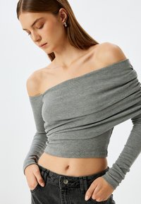 Grauer, schulterfreier, gerippter Oberteil mit langen Ärmeln, mit drapierter Textur. Kombiniert mit hoch taillierten schwarzen Jeans, die eine kontrollierte Passform an der Taille bieten.