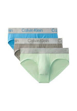 Trzy męskie slipy Calvin Klein w kolorach niebieskim, szarym i jasnozielonym z szarymi, oznakowanymi pasami, ułożone nachodzące na siebie na białym tle.