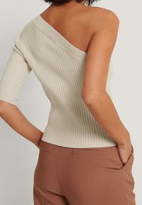 Top beige a costine con design off-shoulder, maniche corte e finitura testurizzata, abbinato a pantaloni marroni con tasche laterali.