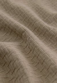 Tissu beige avec un motif géométrique tissé subtil créant un design texturé, légèrement en relief, sur toute la surface.