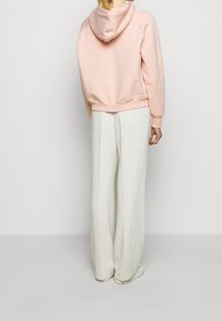 Ljusrosa croppad hoodie med huva, ribbade ärmslut och fåll, i kombination med löst sittande vita byxor. Slät tygtextur.