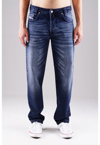 Dunkelblaue Jeans aus Denim mit geradem Schnitt, Ausbleichungen und Kontrastnähten. Getragen mit weißen Sneakers für einen lässigen Look.