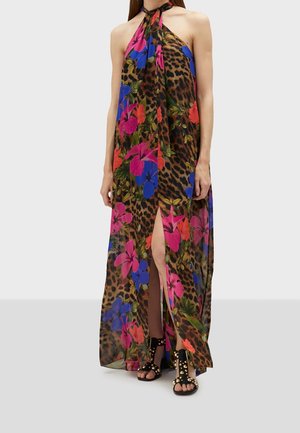 Vrouw draagt een mouwloze maxi-jurk met halternek, leopardprint en levendige blauwe, roze en rode bloemenpatronen, gecombineerd met zwarte sandalen met studs.