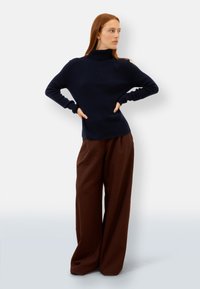 Maglione a collo alto di colore blu navy realizzato in morbido materiale a maglia, abbinato a pantaloni larghi marroni con vestibilità comoda e texture liscia.