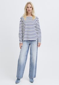 Langærmet, marineblå og hvide stribede bomuldstop, båret sammen med vidbenede lyseblå cowboybukser og matchende blå hælede støvler.