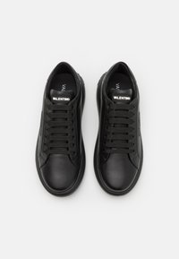 Black leather sneakers with a smooth texture, featuring six lace eyelets, flat shoelaces, and a subtle logo on the tongue.