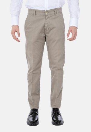 Chinos beige in cotone con taglio dritto, dotati di chiusura con bottone e tasche laterali. Indossati con scarpe nere lucide.