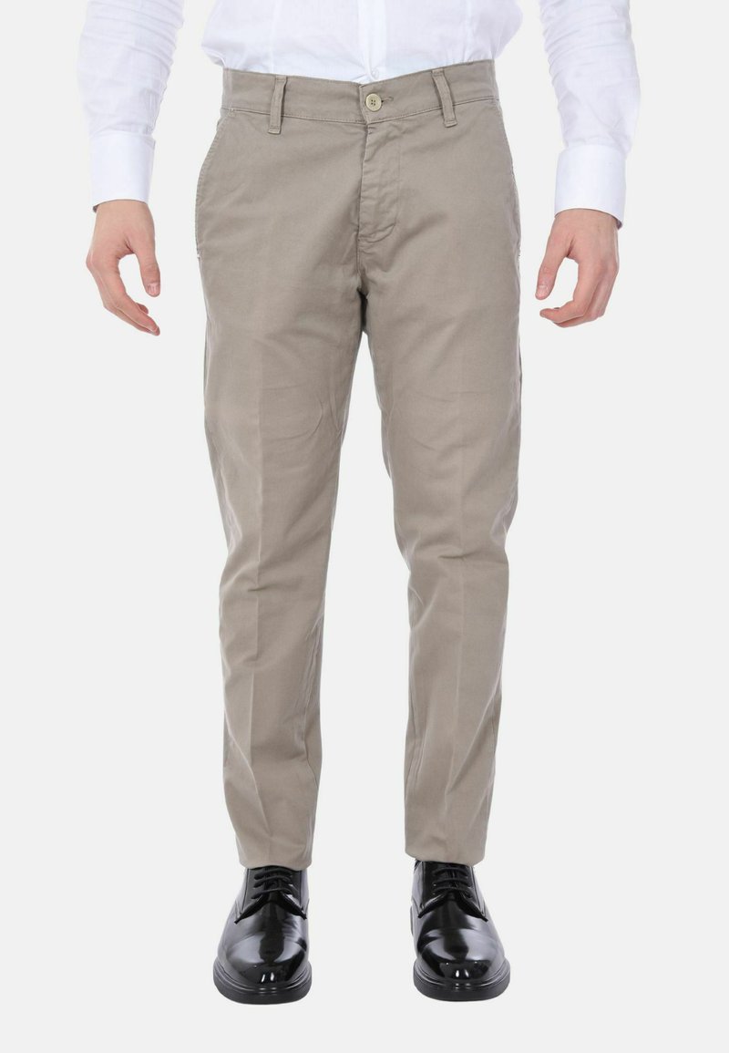 Chinos beige in cotone con taglio dritto, dotati di chiusura con bottone e tasche laterali. Indossati con scarpe nere lucide.