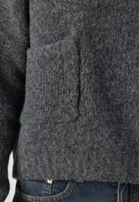 Grijze gebreide trui met een gestructureerd oppervlak, een voorzak en een ontspannen pasvorm. Gecombineerd met denim jeans aan de onderkant.