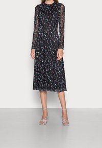 Schwarzes langärmeliges Kleid mit floralem Muster in Pink und Blau; plissierter Rock, transparente Ärmel, runder Ausschnitt, kombiniert mit blauen Riemchenheels.