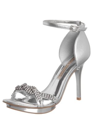 Silberne High-Heel-Sandale mit Knöchelriemen, metallischer Oberfläche, offener Zehenbereich und Strassverzierungen am Zehenriemen. Glatte Textur.