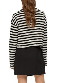 Zwart-wit gestreepte cropped trui in een textuurgebreide stof, met lange mouwen en een raw hem, gecombineerd met een zwarte rok.