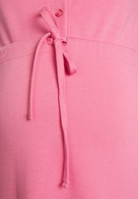 Tecido de vestido rosa com uma textura suave, apresentando um detalhe de cintura atada e um fecho de botão único. O design enfatiza uma silhueta ajustada.