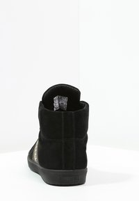 Bottines noires en suede avec une surface texturée, dotées d'un col rembourré et de panneaux latéraux contrastants. Semelle en caoutchouc pour une meilleure adhérence. Taille visible.