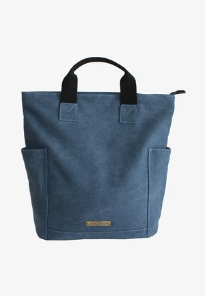 Blue canvas tote bag with black fabric handles, two side pockets, and a metal logo plate. Sturdy design with reinforced stitching.
