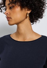 Haut ajusté bleu marine avec un large décolleté, une texture subtile et des manches courtes, associé à des boucles d'oreilles en or.