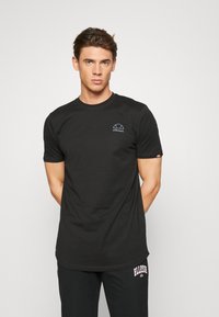 Sort kortærmet t-shirt lavet af bomuld, med et lille gråt logo på brystet og en diskret logo-accent på ærmet.