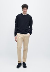 Černý svetr, krémové tričko pod ním, béžové kalhoty a černé tenisky. Ležérní outfit s přiléhavým střihem a hladkou texturou.