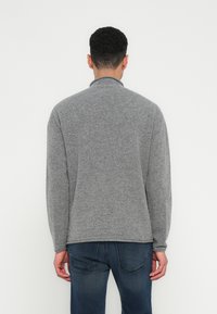 Pulôver cinza de malha com colarinho alto e mangas longas. O tecido parece suave, com uma textura sutil e um corte relaxado. Usado com jeans escuros.