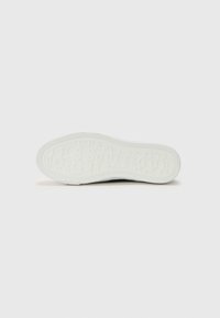 Vit sneakersula med texturerad gummi, med präglat "GUESS"-logomönster och böjda kanter för grepp och flexibilitet.