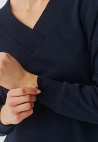 Marineblauwe sweatshirt met een V-hals ontwerp, ribgebreide boorden en gestructureerde stof. Bevat een klein logo op de borst.