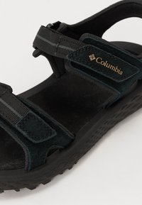 Črne sandale Columbia z antilopovimi trakovi, nastavljivimi Velcro zapiranjem, teksturiranim gumijastim podplatom in mehkimi notranjimi vložki za udobje.