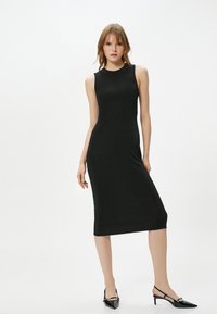 Schwarzes, ärmelloses Midikleid mit enganliegender Silhouette. Glattes Material, schlichtes Design und gerader Saum. Kombiniert mit schwarzen lackierten Slingback-High Heels.