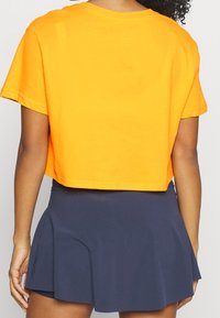 Cropped orange cotton t-shirt with short sleeves, paired with a dark navy flared skirt. Smooth texture, minimal detailing.