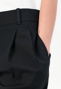 Black pleated trousers with a smooth texture, featuring side pockets and a flat waistband. The fabric appears lightweight and structured.