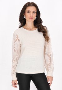 Helles beige Sweatshirt mit strukturiertem Körper und durchsichtigen langen Ärmeln, die mit Blumenstickerei verziert sind. Rundhalsausschnitt und enganliegende Bündchen.