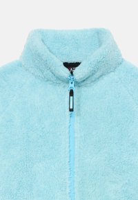 Casaco de polar azul claro com gola alta, fecho frontal completo e tecido suave e texturizado. Apresenta um rótulo interior preto e um fecho de contraste.