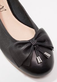Ballet flat en cuir noir avec un détail en nœud aux extrémités métalliques. Bout rond et texture lisse sur le dessus, doublure intérieure douce.