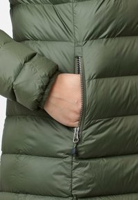 Olivgrüne Steppjacke mit gesteppter Textur und Reißverschlusstasche, ausgestattet mit glattem, glänzendem Außenmaterial und gerippten Bündchen.