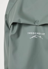 Πράσινο μπουφάν με το λογότυπο Swedemount και γραφικό βουνού, με κουμπί ασφαλείας στο πάνω μέρος.
