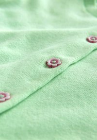 Mintgroene stof met een zachte textuur, voorzien van bloemenvormige roze knopen langs de voorkant voor een detail in het sluitwerk.