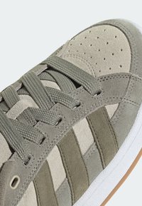 Graue Wildleder-Sneaker mit strukturierten Einsätzen, einer perforierten Zehenpartie, flachen Schnürsenkeln und einer weißen Gummisohle mit einem Kautschukakzent.