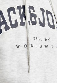 Sudadera gris con "BLACK&JO" impreso en letras azul oscuro. Incluye una capucha con cordón y tela texturizada para mayor comodidad.
