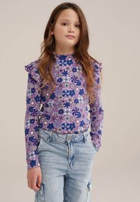 Bluză lungă cu mâneci, de culoare mov, cu un model floral, cu umeri volanati, asociată cu pantaloni cargo de culoare albastru deschis, cu buzunare și o croială relaxată.
