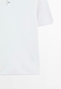 Polo shirt bianca a maniche corte realizzata in tessuto testurizzato, con patta a due bottoni e colletto e maniche a coste.