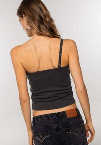 Zwarte getailleerde tanktop met één bandje, versierd met metalen studs. Gepaard met donkerdenim jeans en een leren label met textuur aan de achterkant.