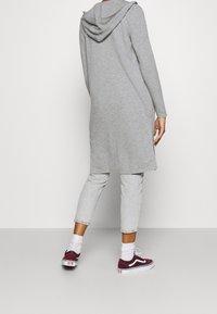 Szary, długi, kapturowy tunik wykonany z miękkiej tkaniny, z długimi rękawami i bocznymi rozcięciami, w połączeniu z jasnoszarymi, krótkimi spodniami oraz burgundowymi trampkami.