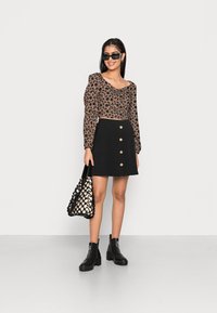 Saia mini preta com botão frontal, combinada com um top cropped floral castanho e botas de tornozelo pretas. Apresenta uma bolsa tecida em preto e branco.