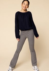 Marineblauwe gebreide lange mouwen top met een gestructureerd patroon; grijze, verticaal gestreepte flared broek. Model staat met handen op de heupen en draagt sneakers.