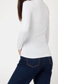 Długorękawowa biała bluzka dopasowana w talii, w połączeniu z ciemnoniebieskimi dżinsami z kontrastowym przeszyciem i tylnymi kieszeniami.