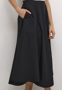 Svart, lång A-linjead kjol i lätt material med hög midja och sidofack; har mjuka veck och en slät yta.