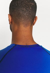 Nike Pro Sportshirt in leuchtendem Blau, mit Rundhalsausschnitt, glatter Textur und schwarzem Stich entlang der Nähte.