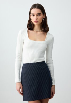 Weißes, geripptes Langarmoberteil mit quadratischem Ausschnitt, kombiniert mit einem mini Rock in dunkelblau mit Nadelstreifen. Sanfte Textur, figurbetontes Design.